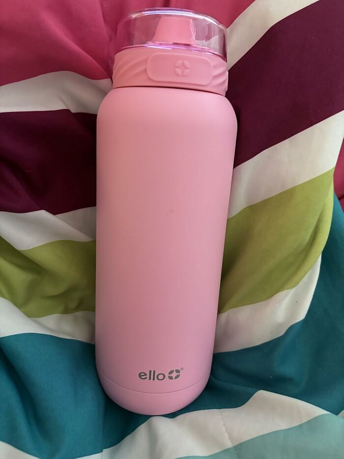 Pink Ello water bottle on colorful bed sheets, illustrating a key heatwave hack for staying hydrated in summer.