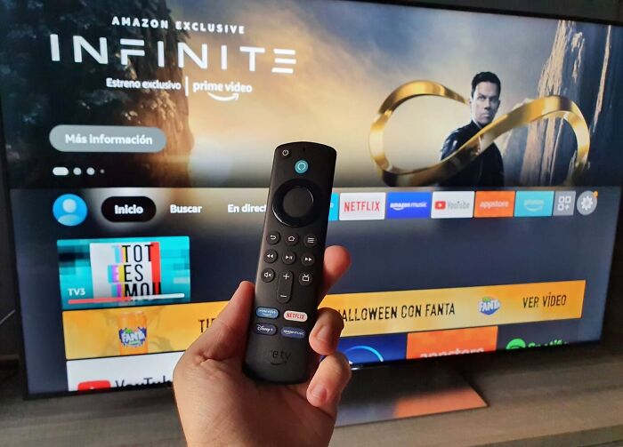 Hand holding a TV remote in front of a smart TV screen showing streaming apps related to best sellers on Prime Day.