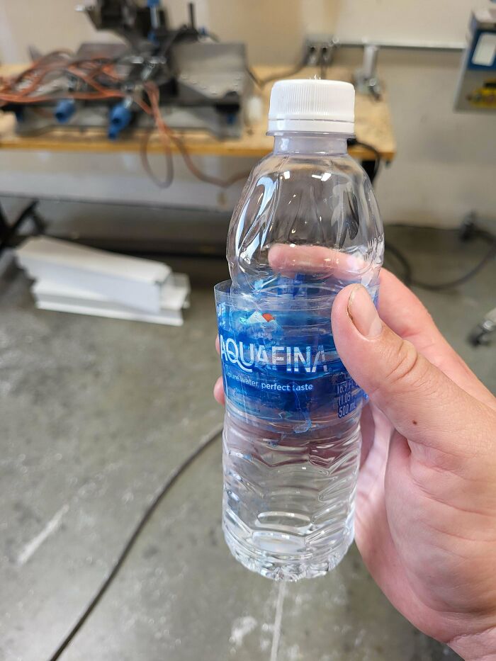 Hand holding a water bottle with a torn label in a workshop, showing an epic work fail in packaging.