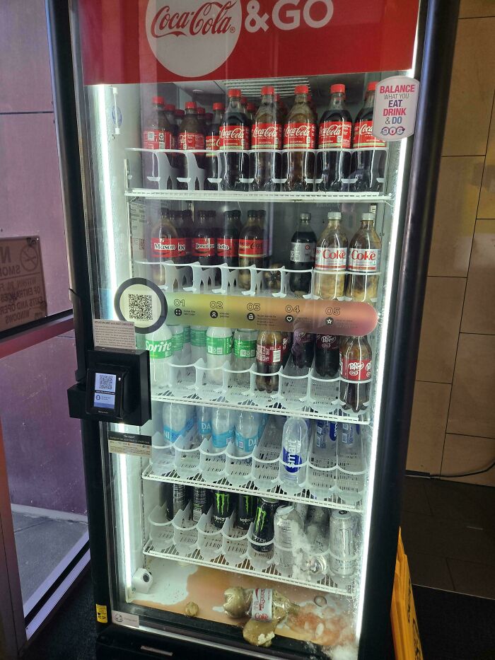 Coca-Cola vending machine with spilled drinks and broken bottles causing a major work fail inside the fridge.