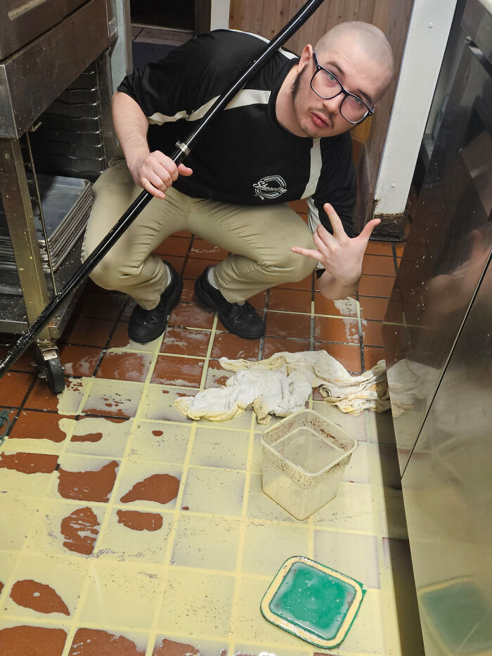 Man cleaning spilled liquid on kitchen floor with mop showing a hand gesture during an epic work fail moment