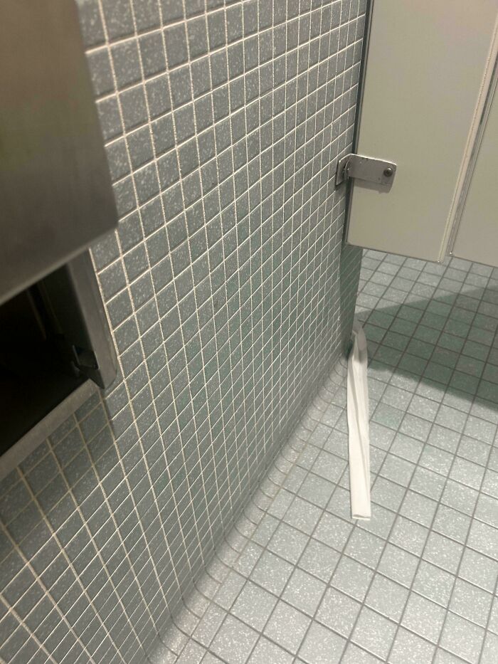 Toilet paper stuck under a bathroom stall door, a common epic work fail in public restrooms.