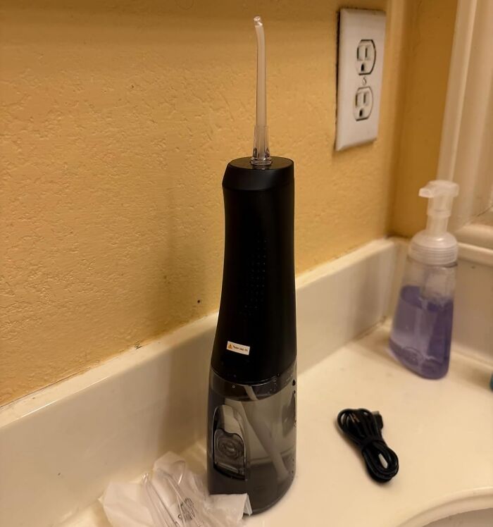 Black water flosser on bathroom counter with soap dispenser and charging cable, one of the top Prime Day finds.
