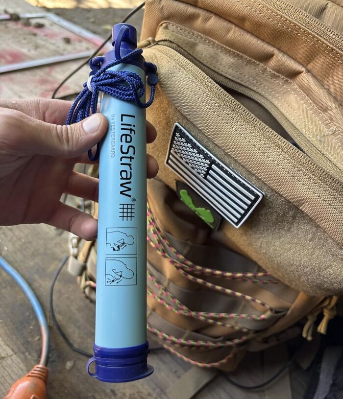Hand holding LifeStraw water filter next to a tan backpack with an American flag patch, prime day finds.