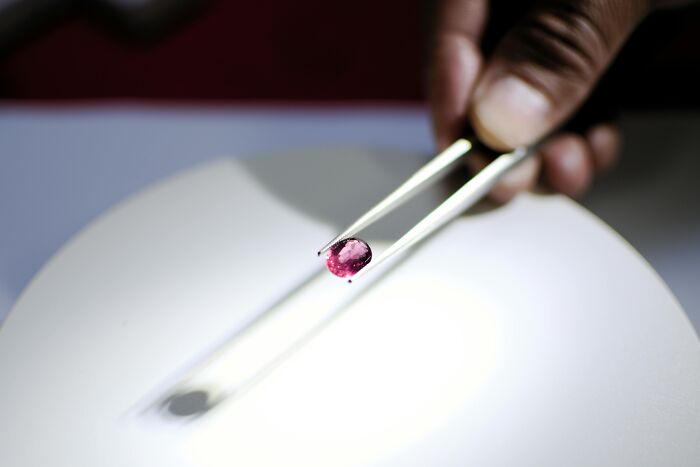 Hand holding a rare pink gemstone with tweezers over a white surface, showcasing highest-value collectible items.