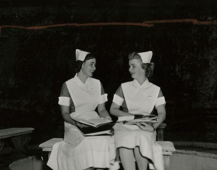 Two vintage nurses in classic uniforms sitting and smiling while holding books, showcasing healing and hope.