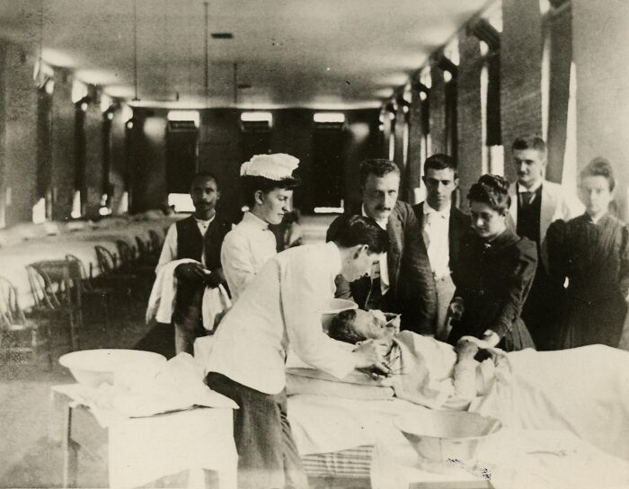 Vintage photo of nurses and doctors caring for a patient in a hospital ward, showcasing early nursing and healing efforts.