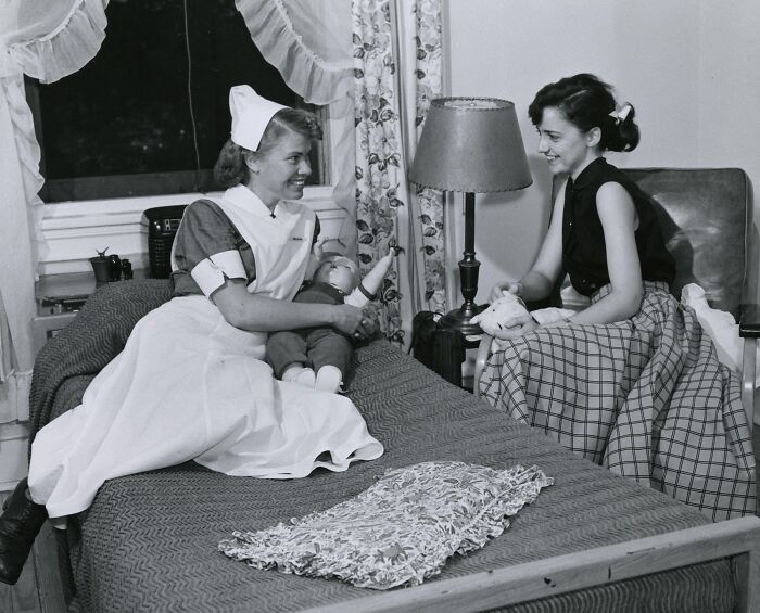 Vintage nurse in uniform caring for a patient doll while sitting on a bed, showcasing classic nursing and healing.