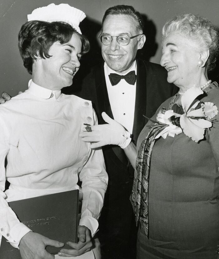 Vintage photo of a nurse smiling with two people at a formal event, showcasing classic nurse healing and hope.