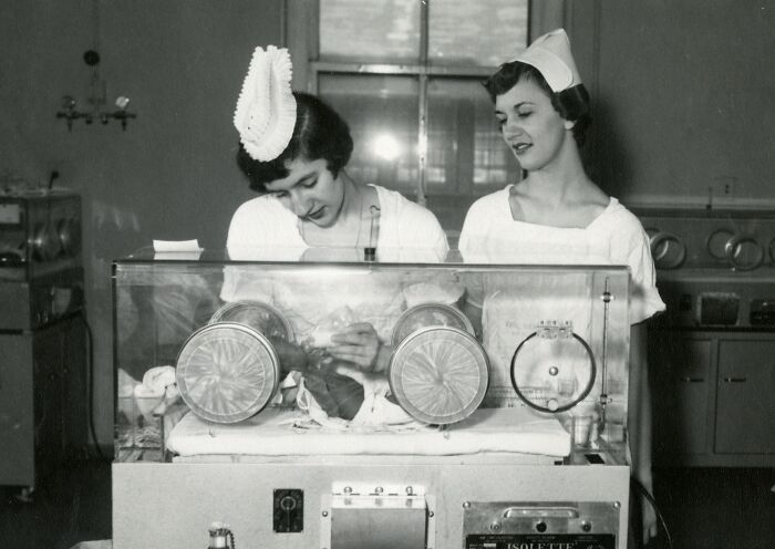 Two vintage nurses caring for a baby in an incubator, showcasing healing and hope in classic nursing attire.