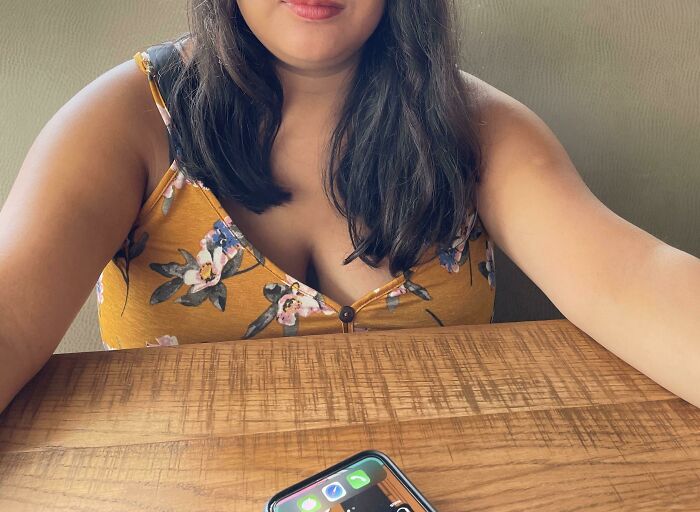 Woman in yellow floral top sitting at a wooden table with phone, representing salon glow-up and emotional breakdown experience.
