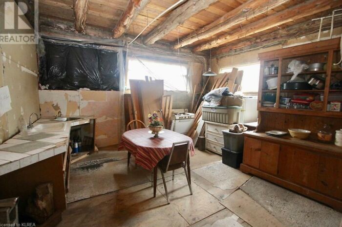 Dilapidated interior of a real estate listing showing unfinished walls, exposed ceiling beams, and mismatched furniture.