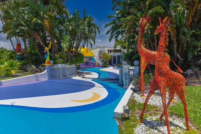 Colorful driveway with bright blue and white paint, vibrant giraffe sculptures, and eclectic outdoor decor in real estate listing.