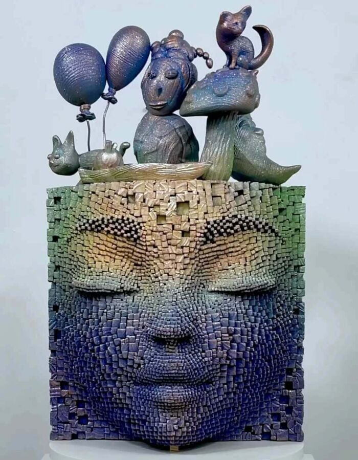 Wooden sculpture featuring a hypnotic 3D face with intricate pixelated texture and small animal figures on top.