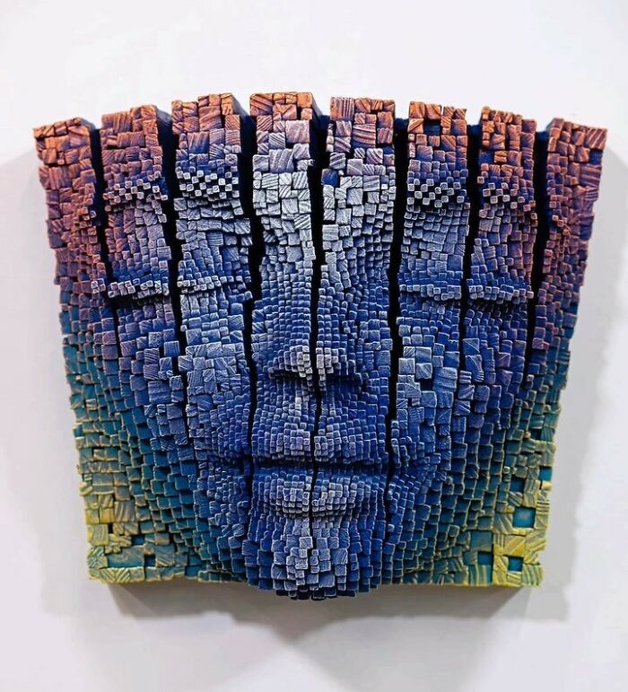 3D wooden face sculpture made of small carved sticks in blue and yellow tones with a hypnotic, lifelike expression.