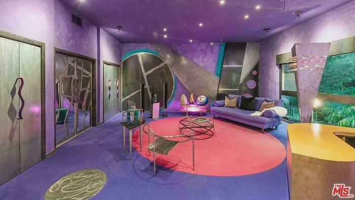 Eclectic real estate listing interior with bold purple walls, geometric patterns, and unusual modern furniture and decor.