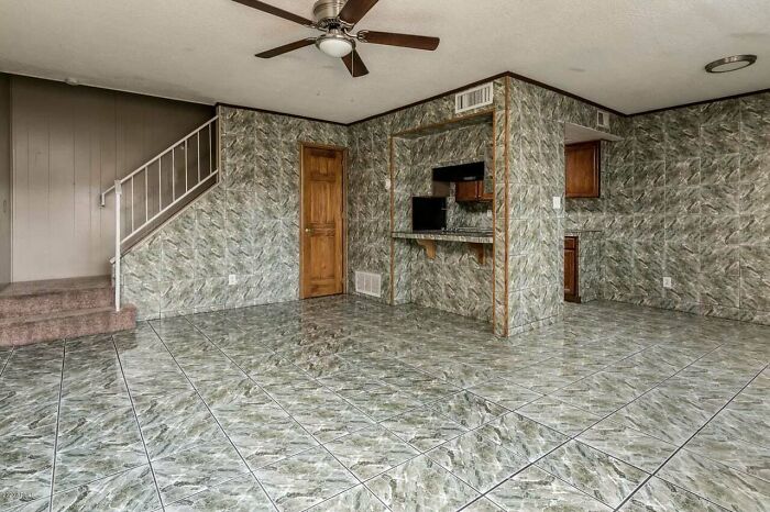 Room with uniform patterned tile floor and walls, wooden doors, and a ceiling fan in an unhinged real estate listing.