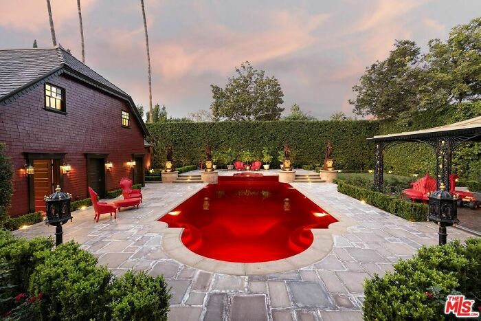 Luxury real estate listing with a bright red pool and eclectic outdoor seating in a well-manicured backyard.