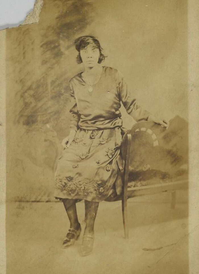 Vintage postcard photo of a 1930s woman in period dress seated beside a chair, capturing the heart of the era.