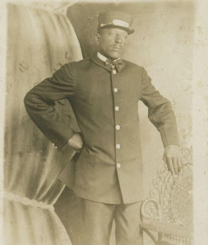 Vintage postcard photo of a man in 1930s uniform posing beside an ornate chair, capturing vintage postcards charm.