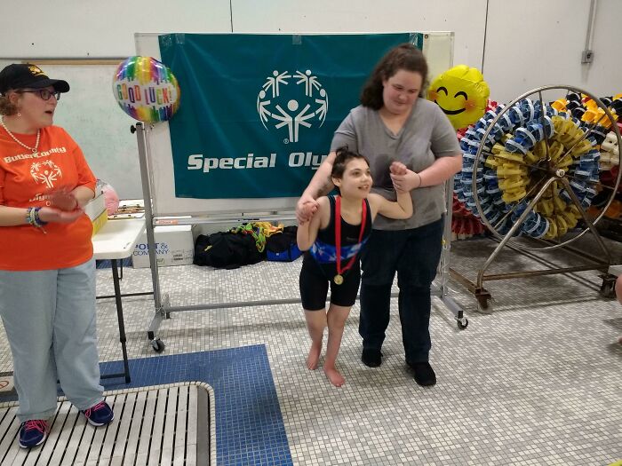 Young athlete with medal celebrating unbelievable luck at Special Olympics event, supported by a smiling caregiver.