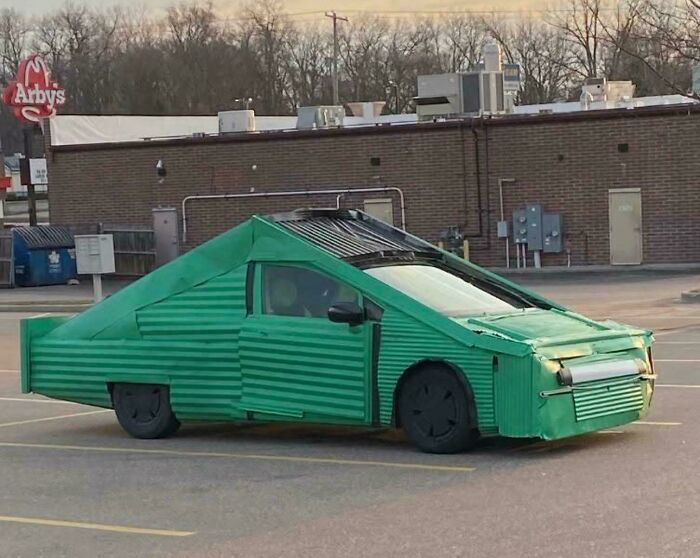 Green car with an outrageous custom corrugated metal exterior parked in a lot showing extreme car mods.