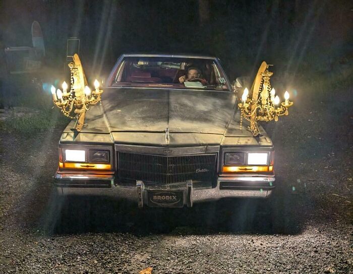 Vintage car with two ornate chandeliers mounted as lights on the hood, showcasing outrageous car mods at night.