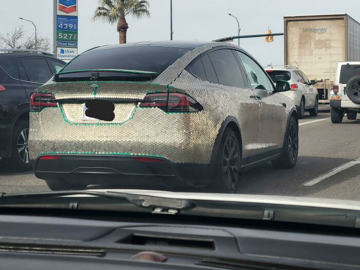Electric car fully covered with shiny metallic scales modification on a city street, an outrageous car mod seen in traffic.