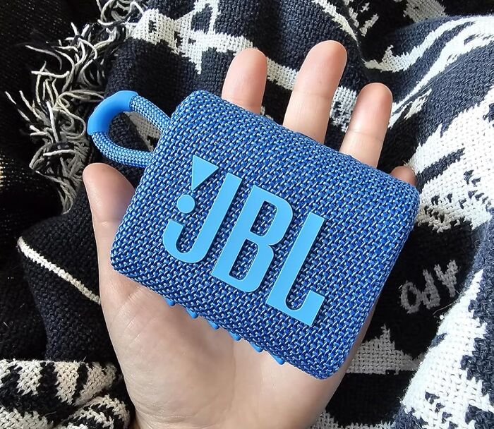 Blue JBL portable speaker held in hand against a black and white patterned fabric, showcasing Prime Day electronic deals.