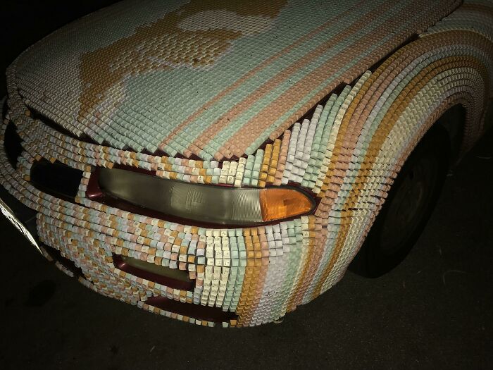 Front side of a car covered in small colorful tiles showcasing one of the most outrageous car mods at night.