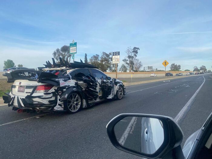 Car with outrageous car mods featuring large spikes and extreme body modifications parked by the side of a highway.