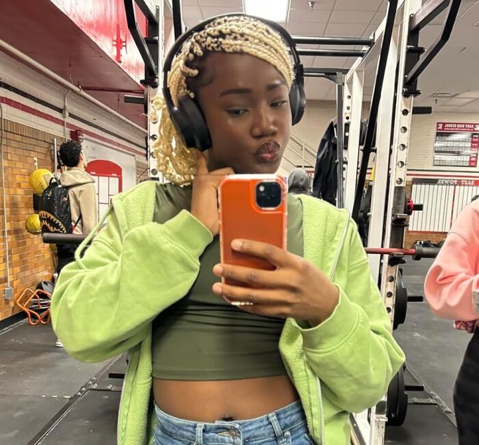 Young woman with headphones taking a selfie at the gym using a smartphone, showcasing electronic deals and modern tech accessories.