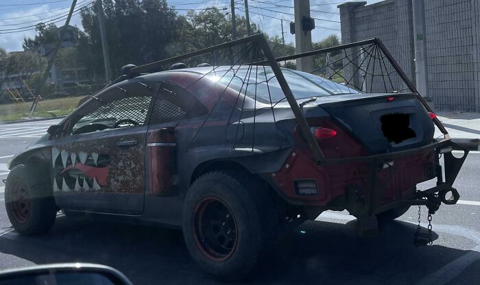 Custom off-road car with shark teeth decals and large spider web frame mod on the back, an example of outrageous car mods.