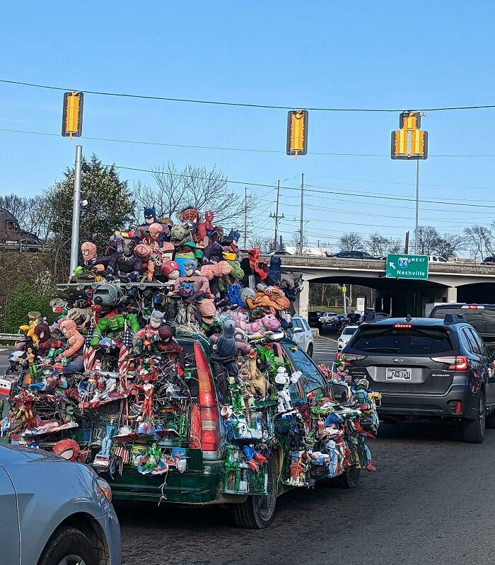 Car covered in outrageous car mods with numerous action figures and toys attached, creating an extreme visual overload.