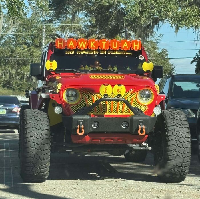 Brightly customized red Jeep with oversized tires and unique yellow accents showcasing outrageous car mods on a city street.
