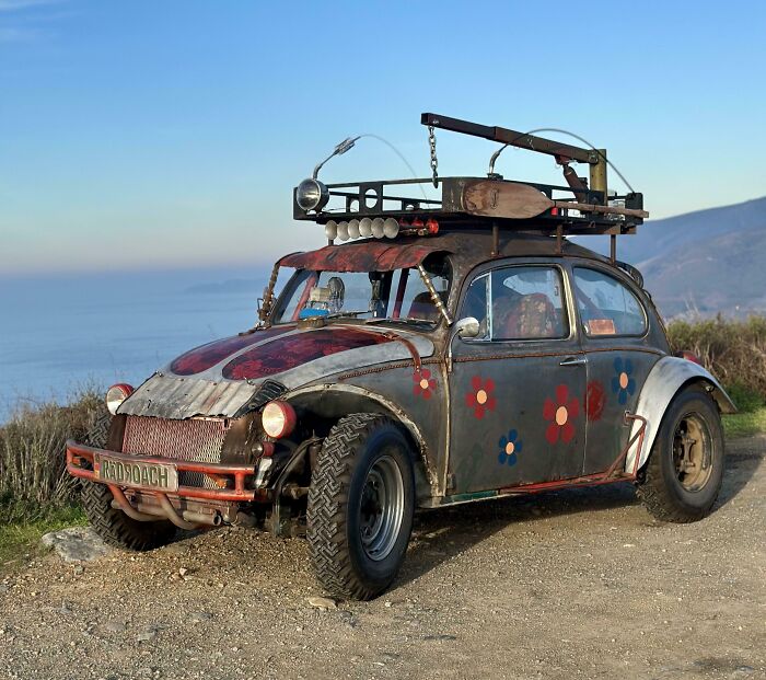 Outrageous car mods on a vintage car with rugged tires, roof attachments, and a weathered, customized exterior.