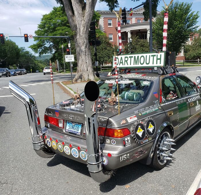 Outrageous car mods featuring oversized exhaust pipes, spikes on wheels, and numerous stickers on a gray sedan.