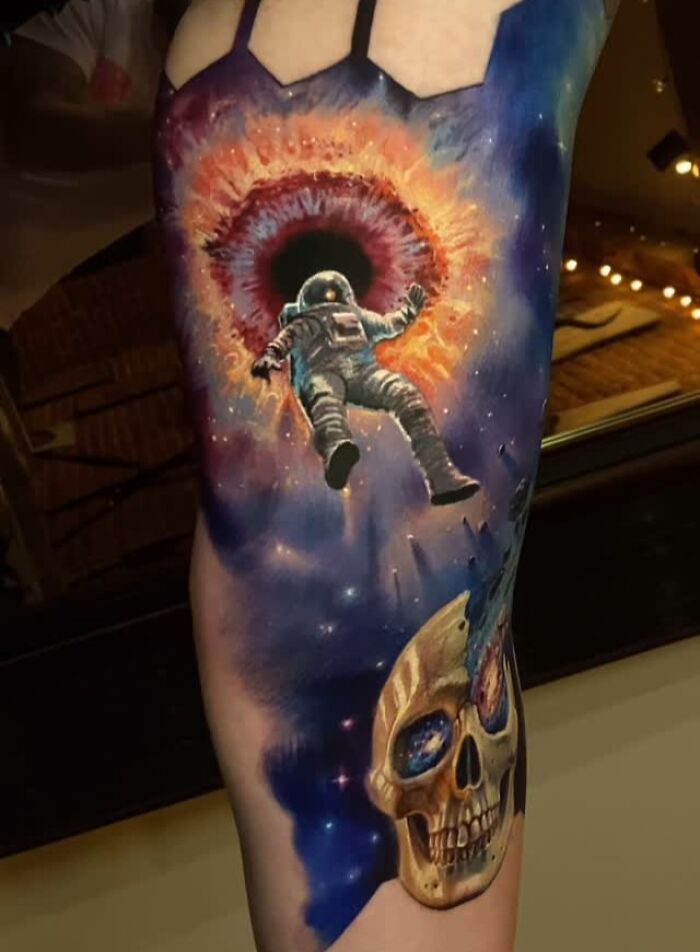 3D tattoo of astronaut floating toward a cosmic portal above a skull with space-themed design on arm.