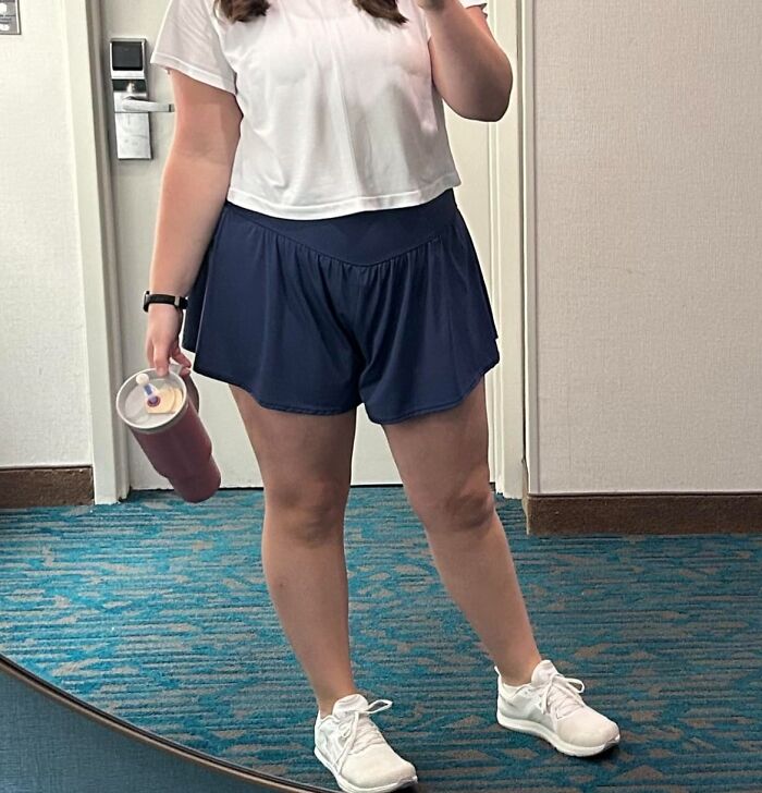 Person wearing a white shirt and navy shorts holding a drink, illustrating comfortable casual style under $25 deals.