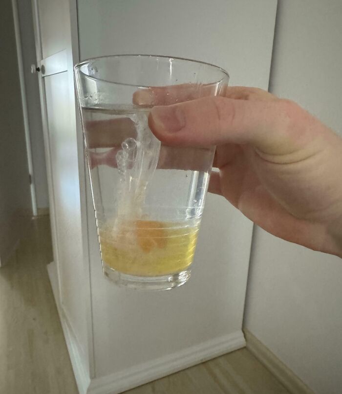 Hand holding a glass of water with an eggshell and egg yolk mixed inside, showcasing clueless partner humor.