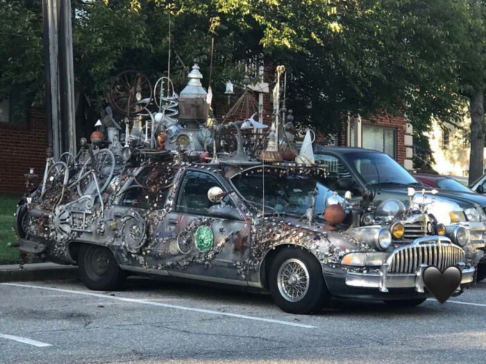 Car covered in outrageous car mods with various objects and decorations attached, parked in a residential area.