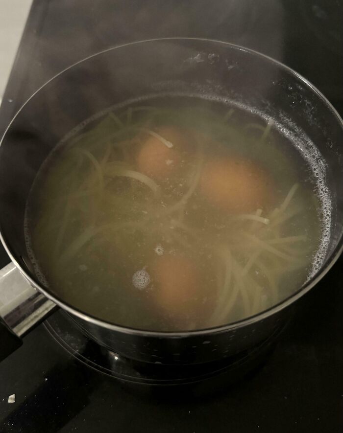 Pot with boiling water containing uncooked spaghetti and whole eggs, showcasing a clueless partner cooking fail.