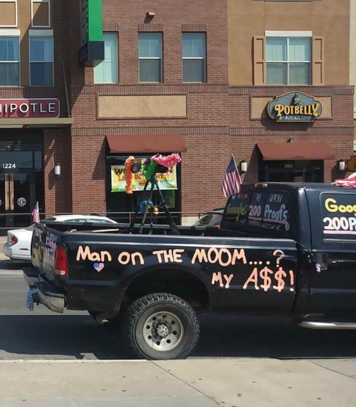 Pickup truck covered with outrageous car mods and humorous handwritten text parked on a city street.
