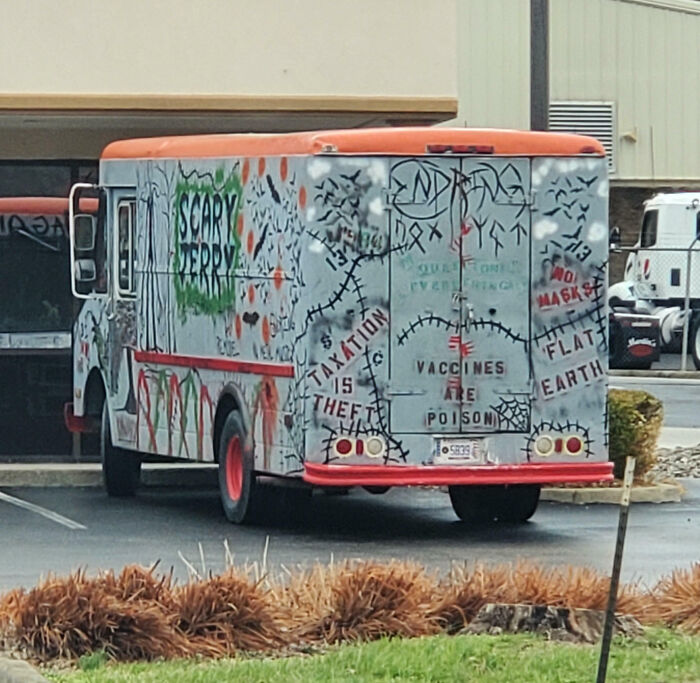 Outrageous car mods on a delivery truck covered in graffiti with phrases and colorful paint designs in a parking lot.