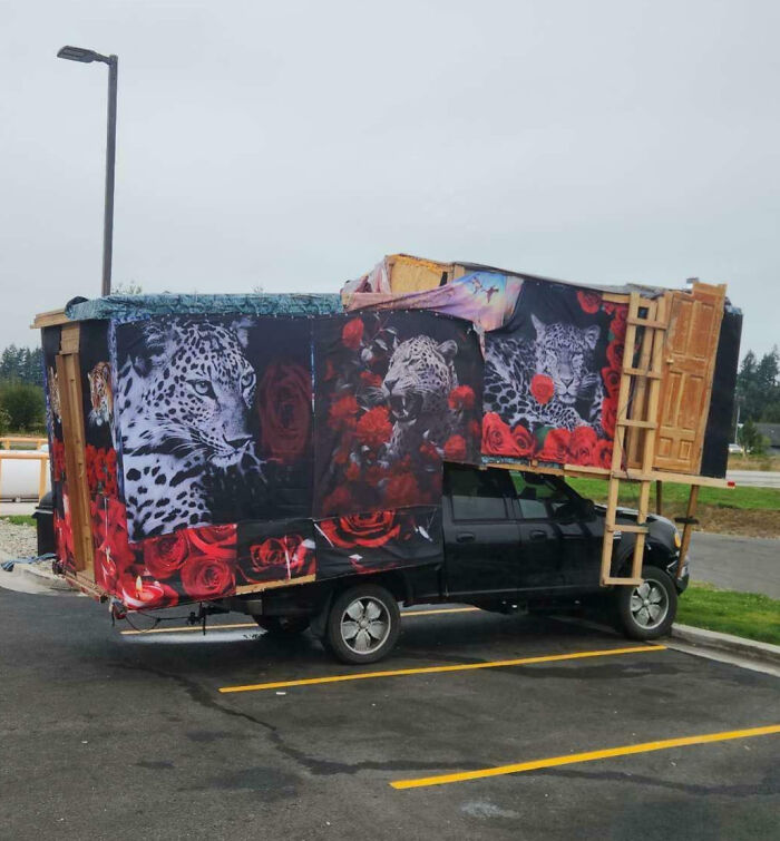 Truck with outrageous car mods features large wooden structure covered in leopard and rose prints extending over the vehicle.