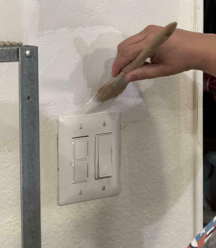 Hand painting the wall with a brush covering a light switch, a funny example of clueless partners in photos.