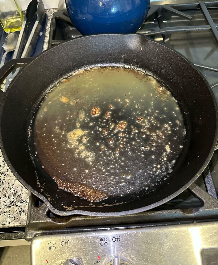 Burnt cast iron skillet on stove with melted and bubbling residue, showcasing clueless partner cooking fail.