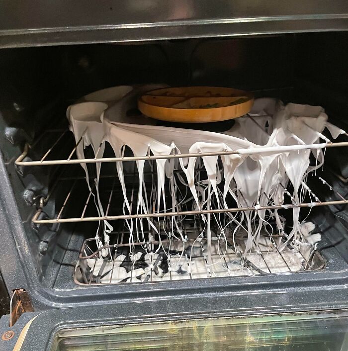 Oven interior with melted plastic hanging from racks, showing a clueless partner's cooking mistake in a messy kitchen fail.