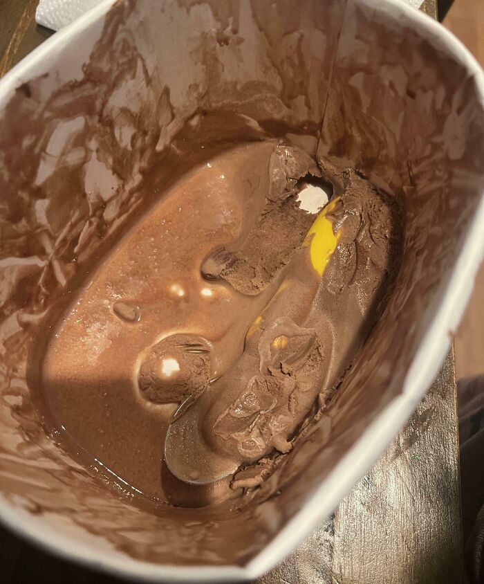 Partially eaten chocolate ice cream with a whole egg yolk inside, showing a clueless partner's funny mistake.