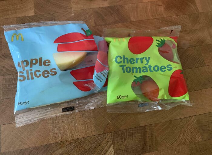 Two snack packs labeled apple slices and cherry tomatoes on a wooden surface, showing clueless partners' funny mix-up.